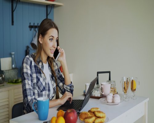 Woman working on laptop at kitchen table with soft morning light